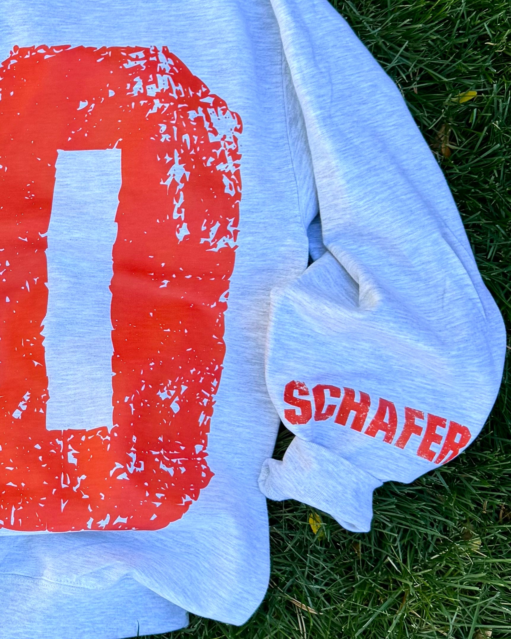 Light blue sweatshirt with a large red number '0' and the name 'SCHAFFER' on grass.