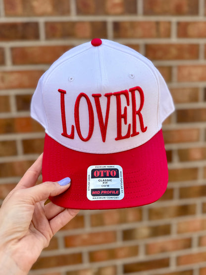 Red and white cap with 'LOVER' text held against a brick wall