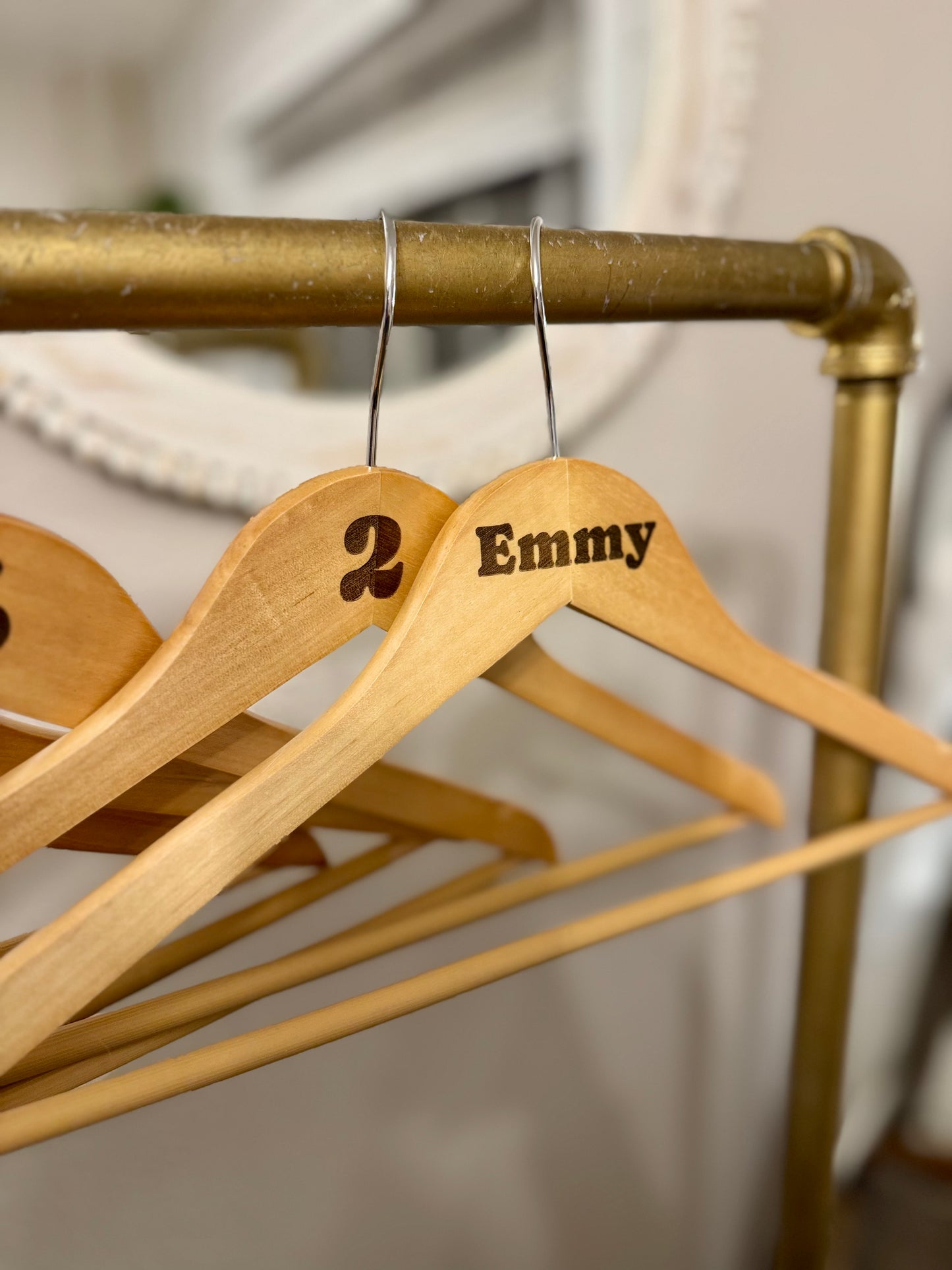 Wooden hangers with 'Emmy' and '2' on a gold rack.