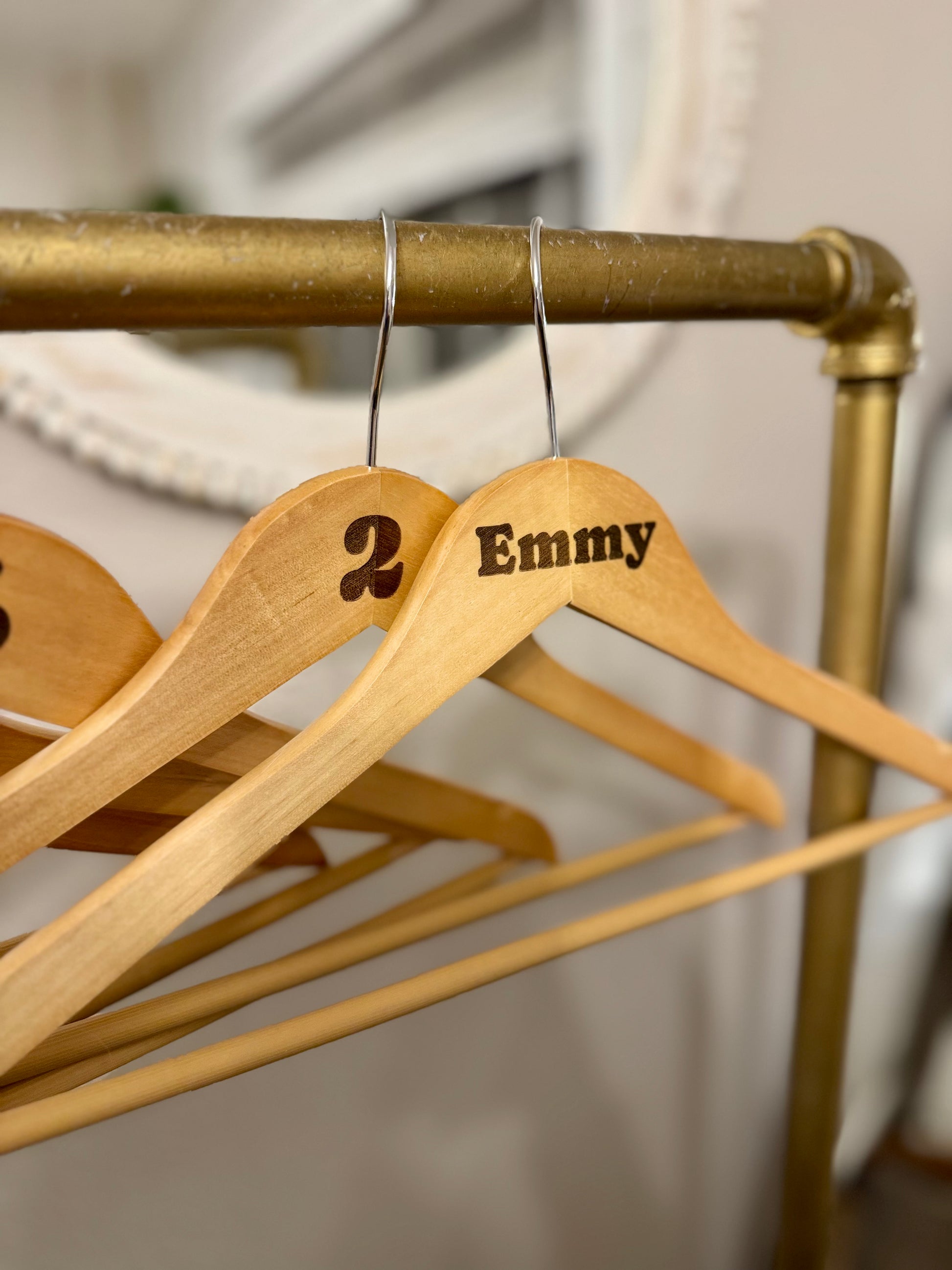 Wooden hangers with 'Emmy' and '2' on a gold rack.