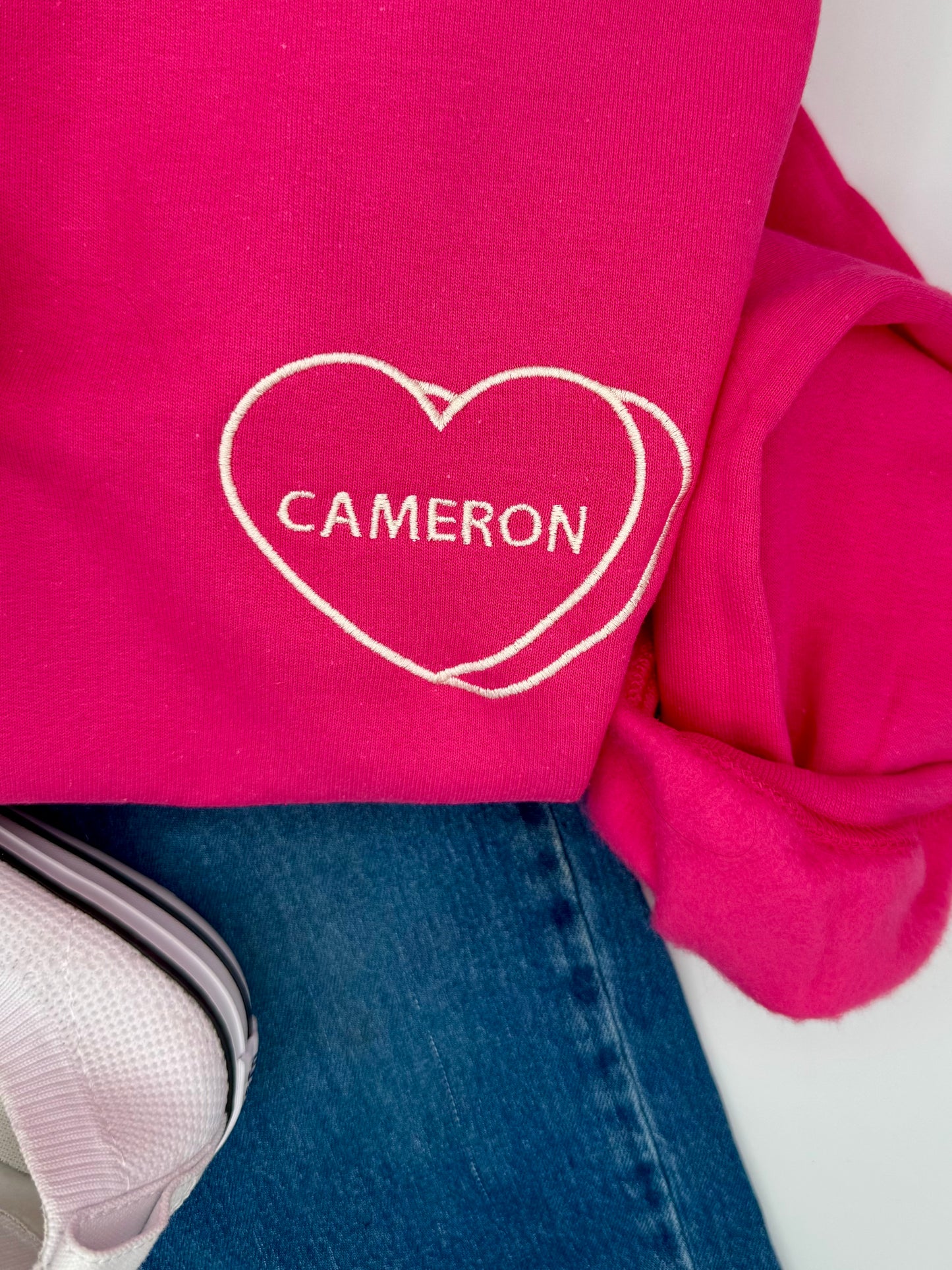 Pink sweatshirt with 'Cameron' in a heart shape on a white background
