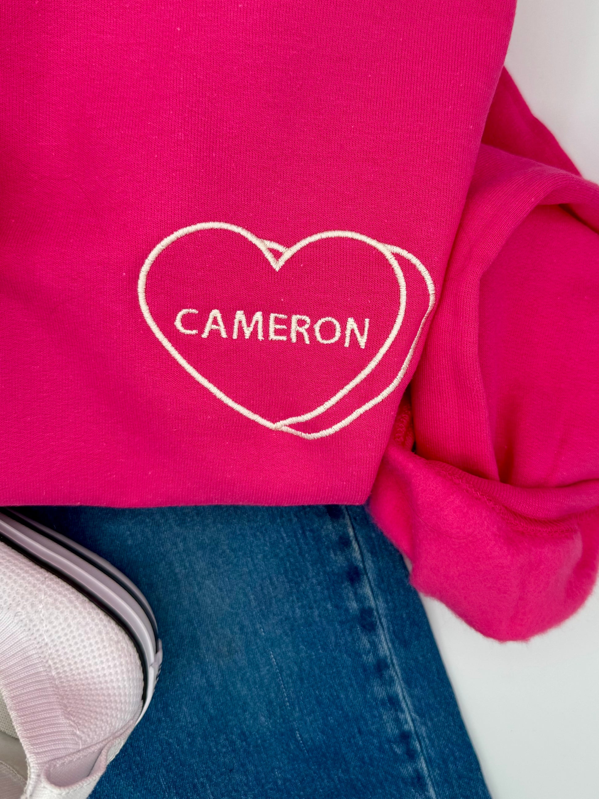 Pink sweatshirt with 'Cameron' in a heart shape on a white background