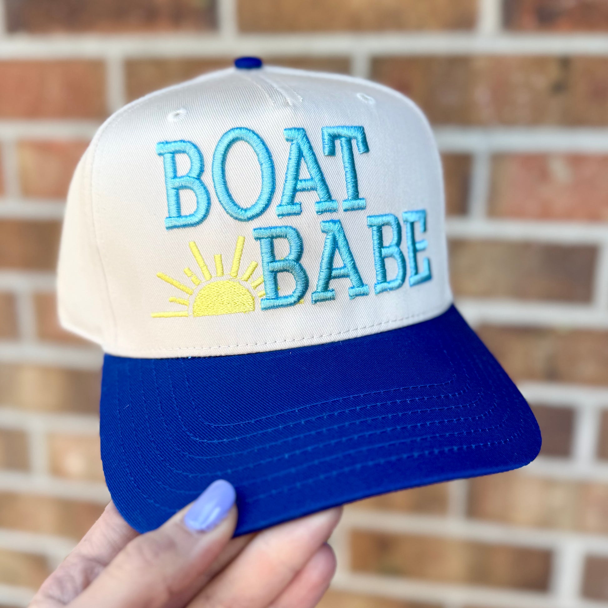 Cap with 'BOAT BABE' text held against a brick wall