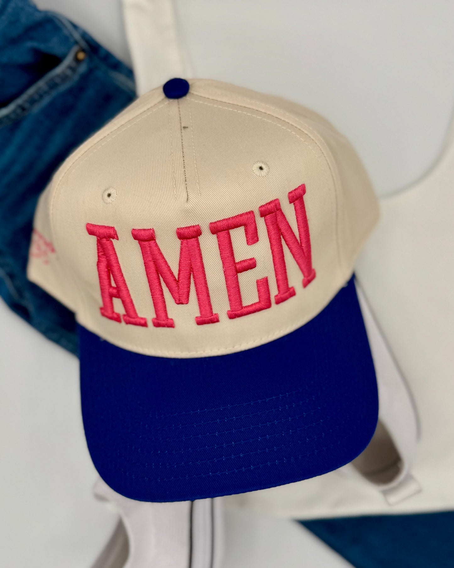 Beige and blue cap with 'AMEN' in pink on a white background