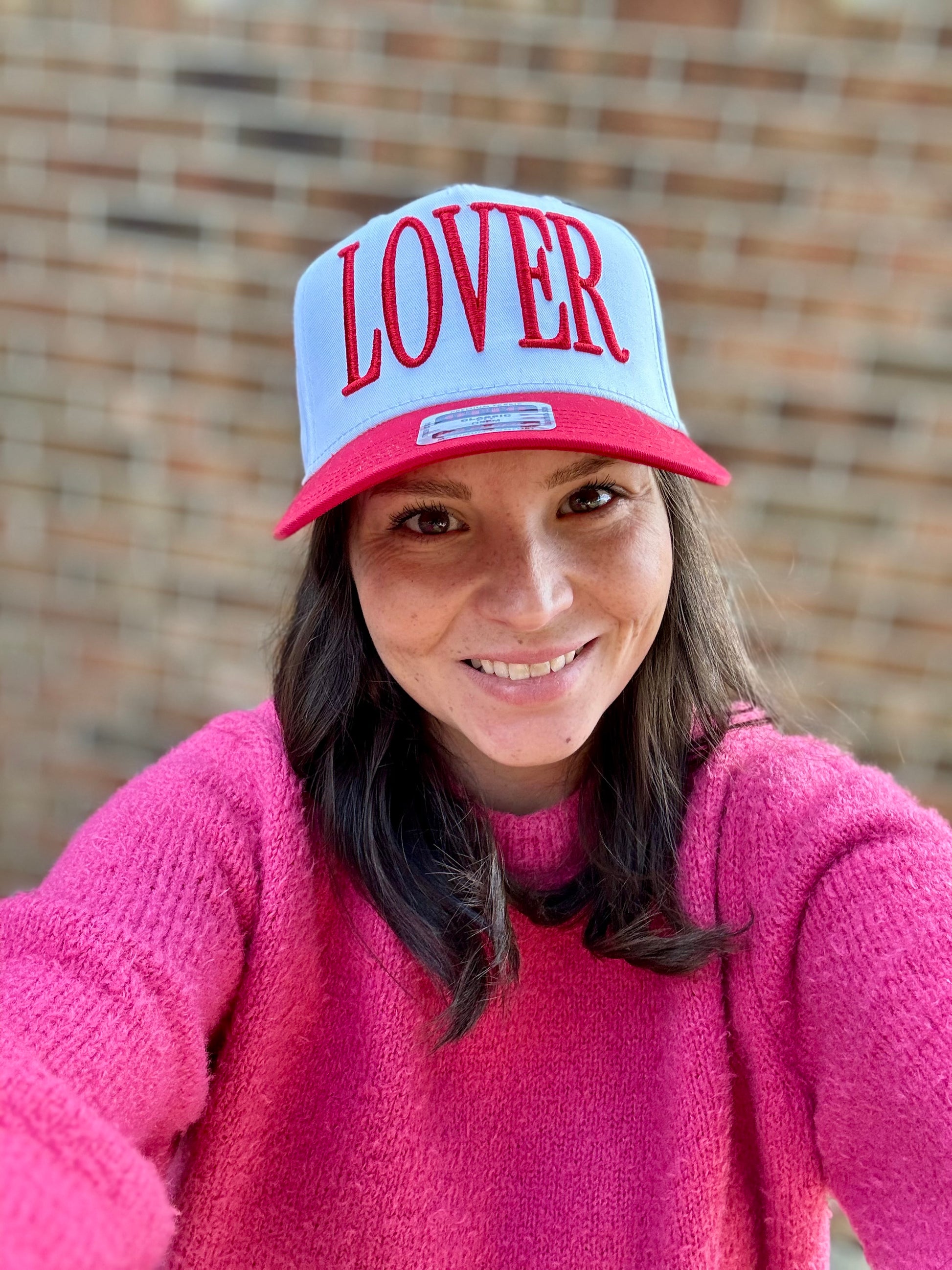 Person wearing a white and red cap with 'LOVER' text, smiling outdoors.