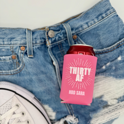 Pink can cooler with 'THIRTY AF' text on denim jeans and a white sneaker.