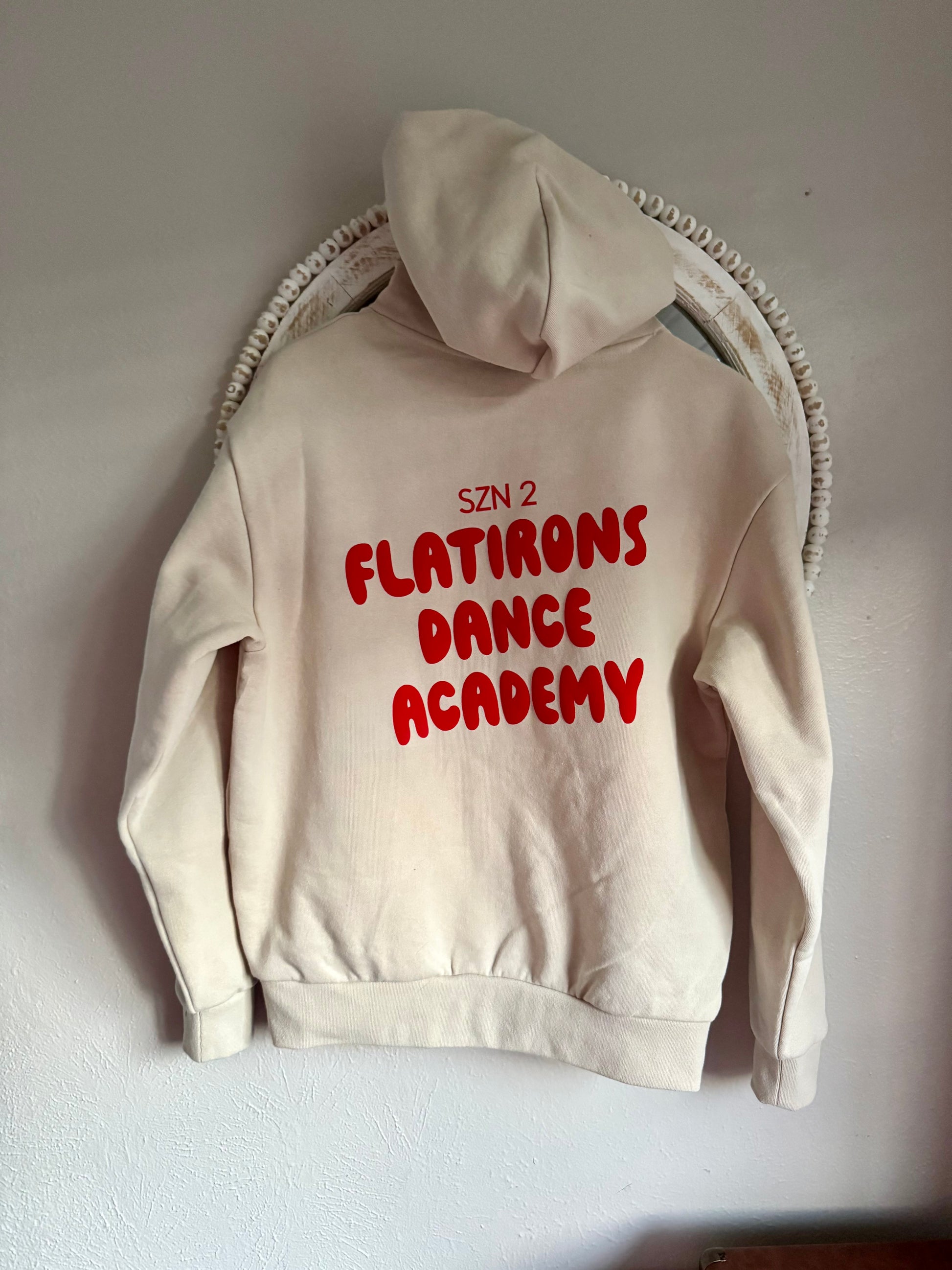 Beige hoodie with red text 'SZN 2 FLATIRONS DANCE ACADEMY' on a white background