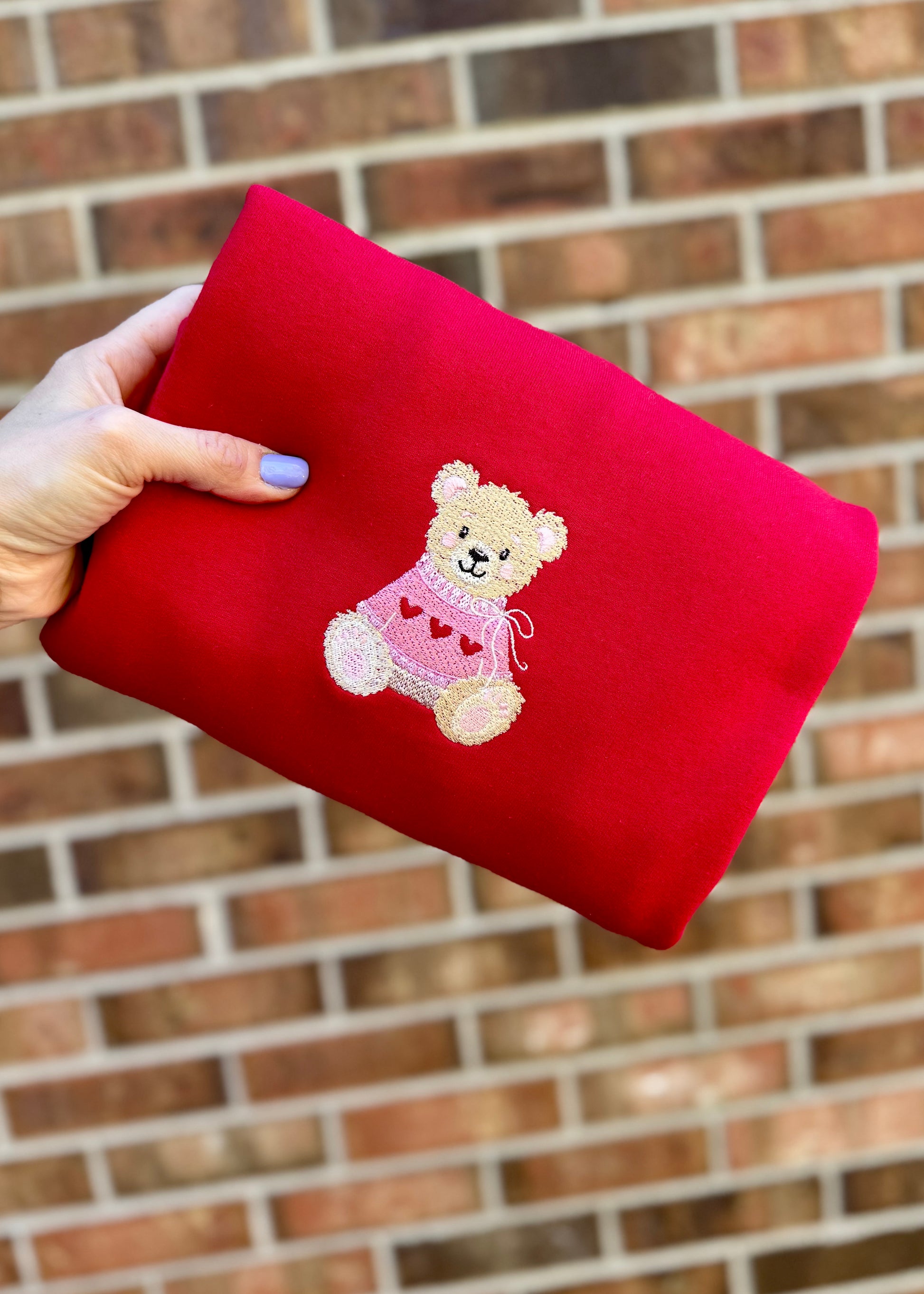 Red pouch with a teddy bear design held against a brick wall.