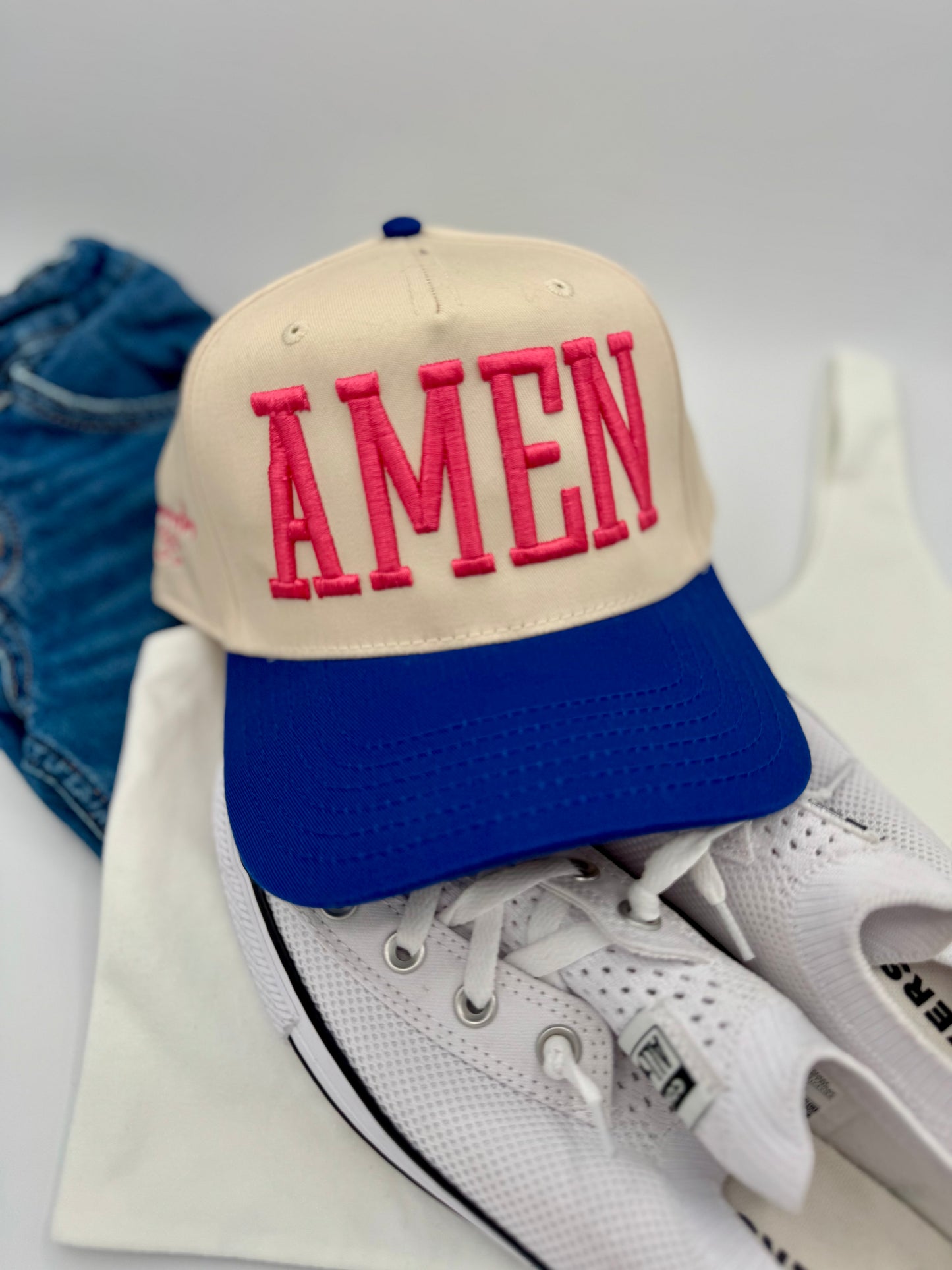 Beige cap with 'AMEN' in red on a white sneaker with blue accents