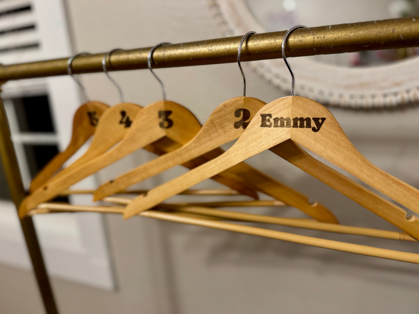 Wooden hangers with numbers and names on a brass rod against a neutral background
