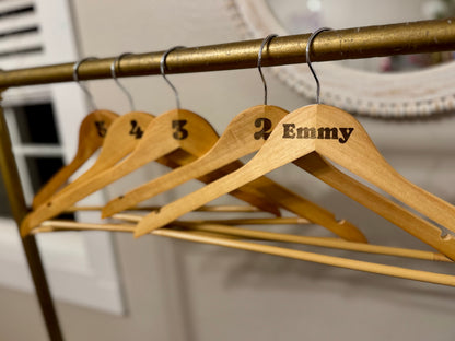 Wooden hangers with numbers and names on a brass rod against a neutral background