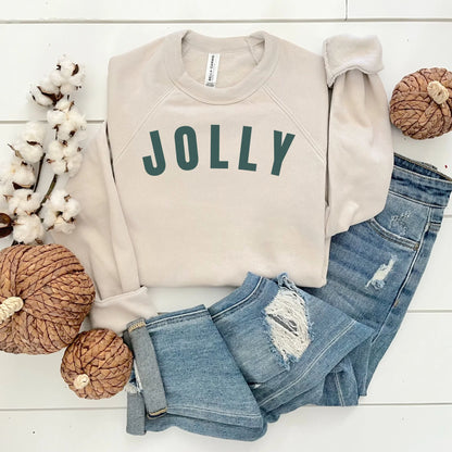 Beige sweatshirt with 'JOLLY' text, blue jeans, and decorative items on a white surface