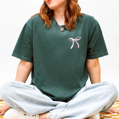 Person wearing a green t-shirt with a pink bow design on a white background