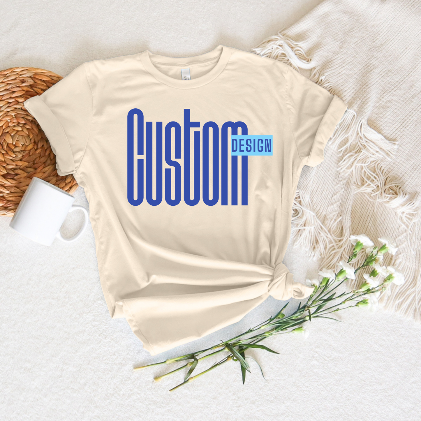 Beige t-shirt with 'Custom Design' text on a white surface with a mug and flowers.