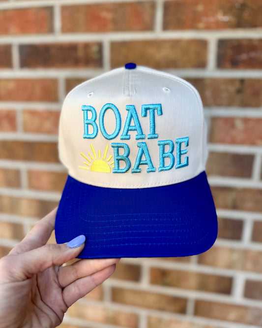 Blue and white cap with 'BOAT BABE' text held against a brick wall.