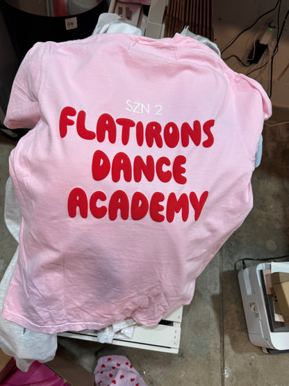 Pink shirt with red text 'Flatiron Dance Academy' on a table.