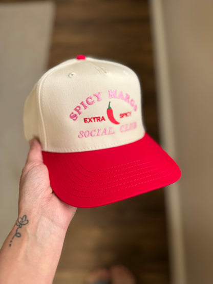 Beige and red cap with 'Spicy Mango Extra Social Club' text held by a hand.