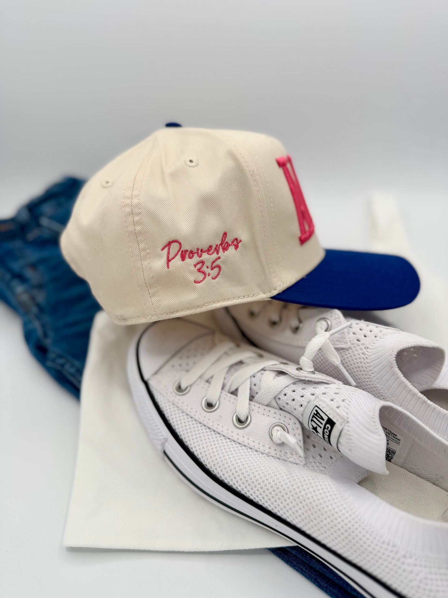 White sneakers, beige cap with red text, and blue jeans on a light gray background
