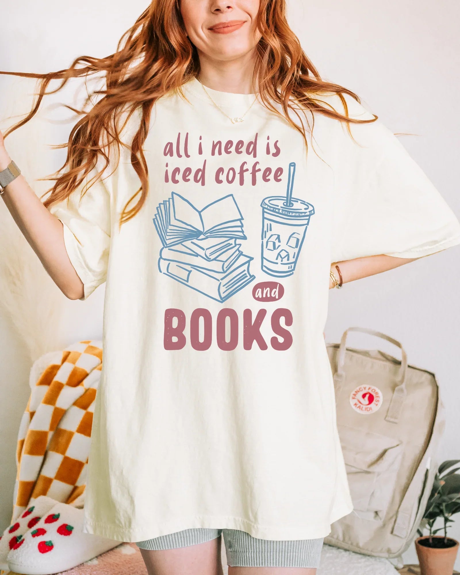 Person wearing a white t-shirt with a graphic and text 'all i need is iced coffee and books' in a casual setting.