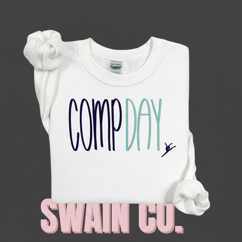 White sweatshirt with 'COMP DAY' and a dancer graphic embroidered on a light pink background