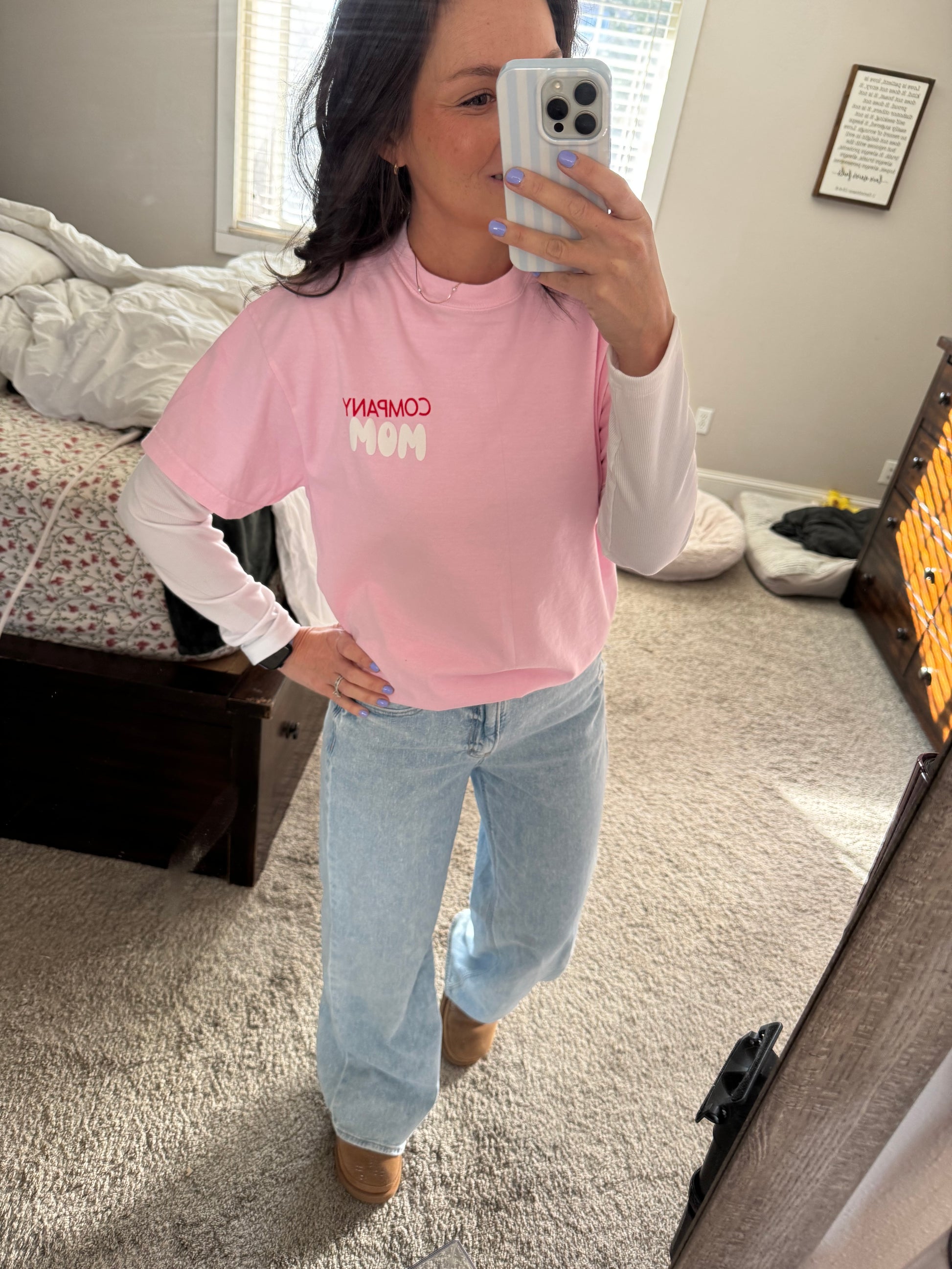 Person wearing a pink sweatshirt with text, taking a mirror selfie in a room.