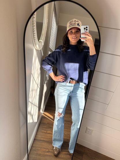 Person taking a mirror selfie wearing a blue sweater, light blue jeans, and a beige cap.