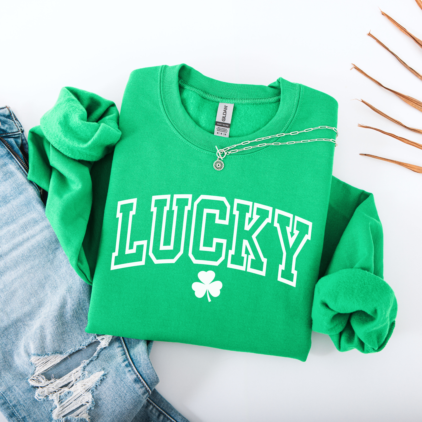 Green sweatshirt with 'LUCKY' and clover design on a white surface with denim jeans.