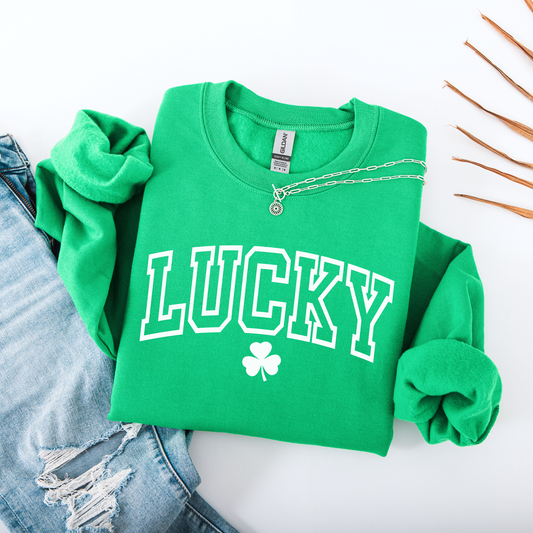 Green sweatshirt with 'LUCKY' and clover design on a white surface with denim jeans.
