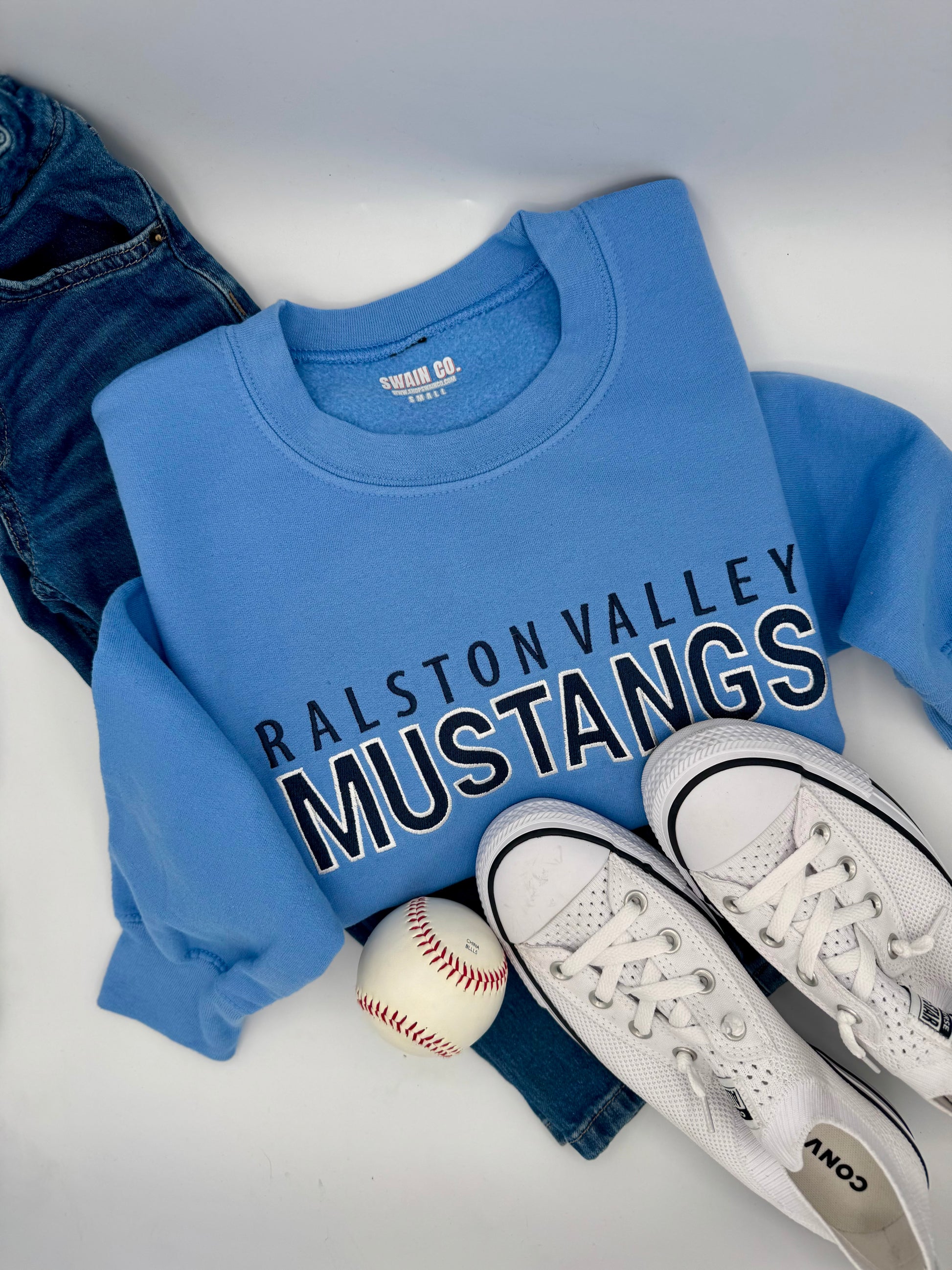 Blue sweatshirt with 'Ralston Valley Mustangs' text, white sneakers, and a baseball on a light gray background