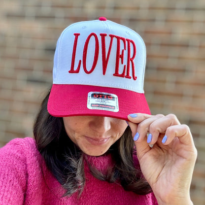 Person wearing a red and white cap with 'LOVER' on it, holding it over their face.