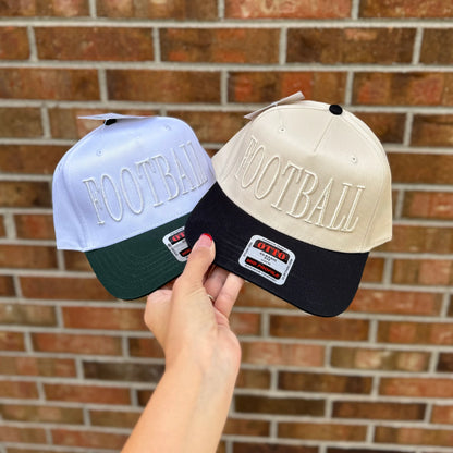 Two baseball caps with 'FOOTBALL' text held against a brick wall.