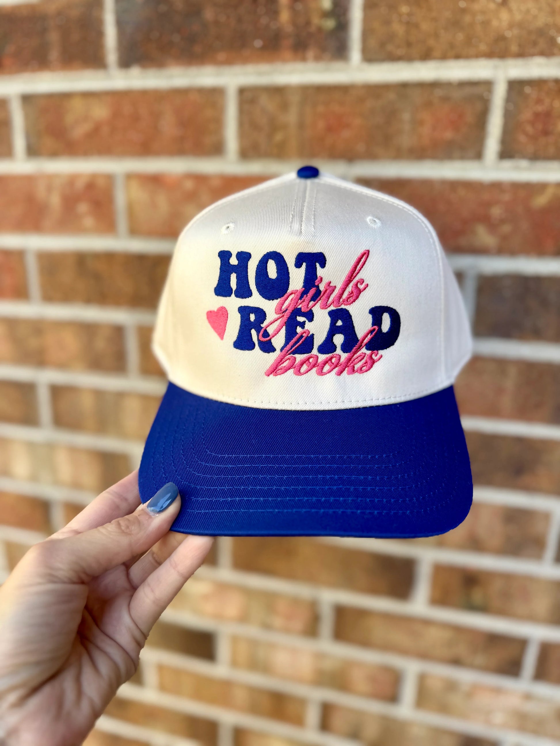 Cap with 'Hot girls read books' text held in front of a brick wall