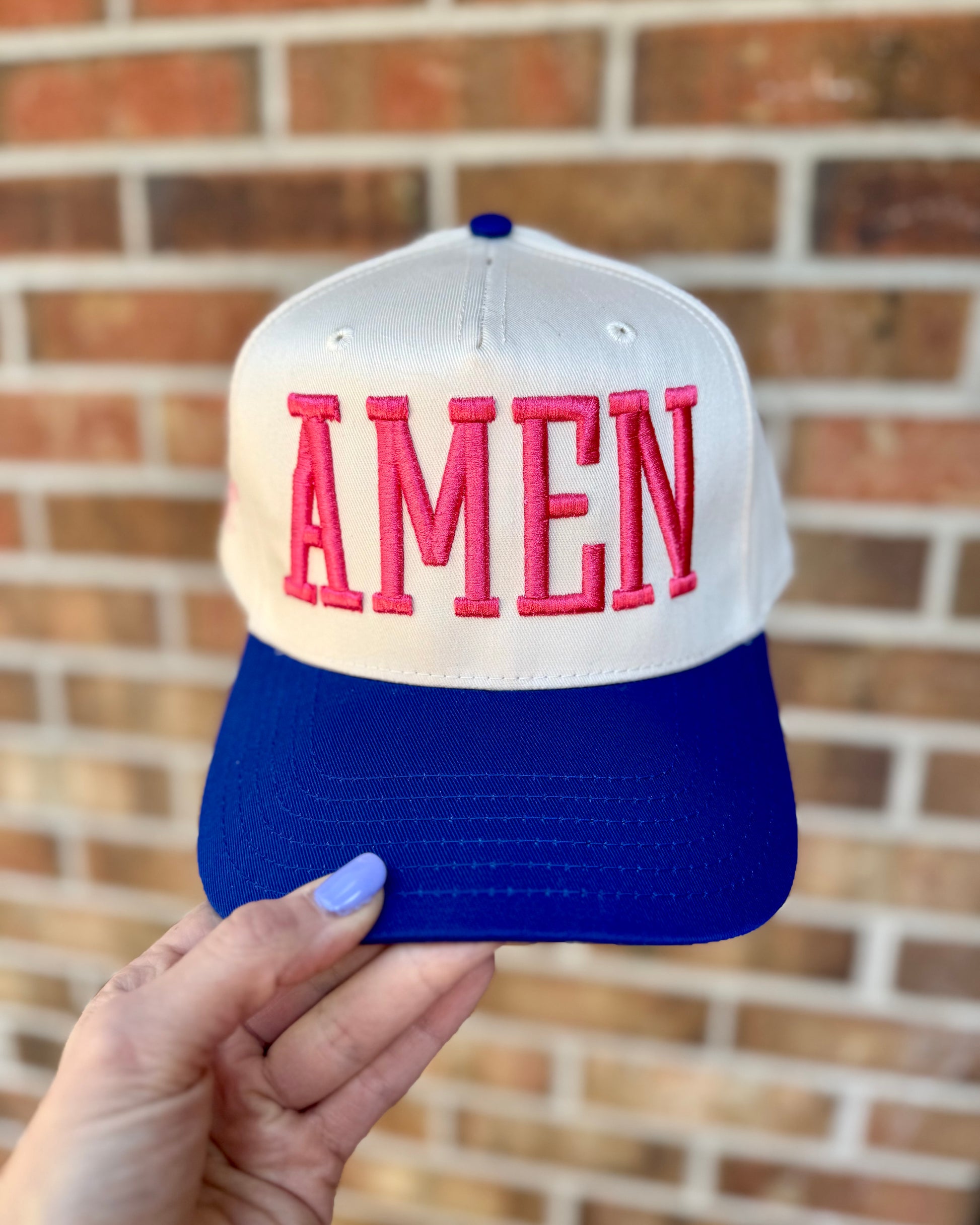 Cap with 'AMEN' text held in front of a brick wall