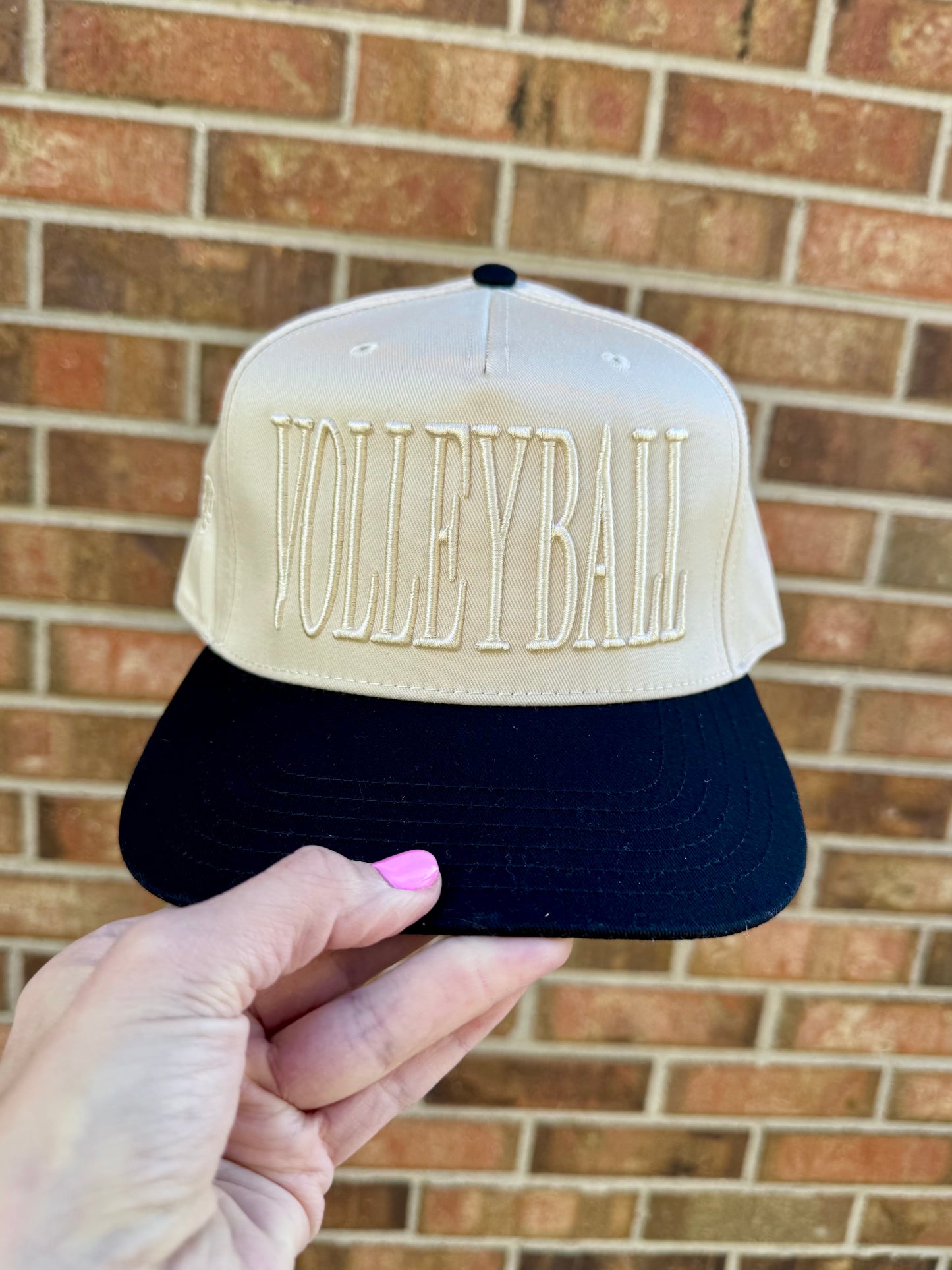 Cap with 'Volleyball' text held in front of a brick wall