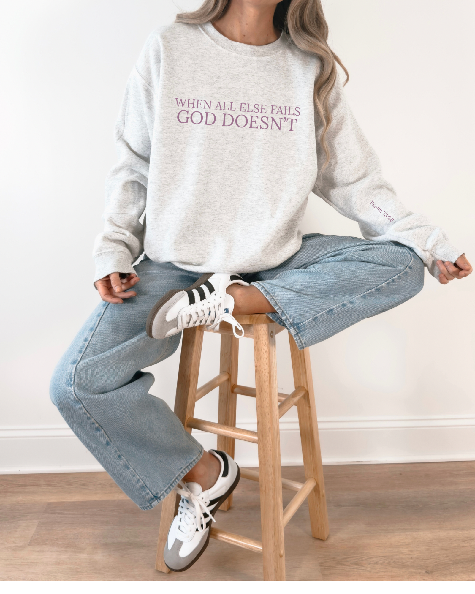 Person wearing a gray sweatshirt with text, sitting on a wooden stool.
