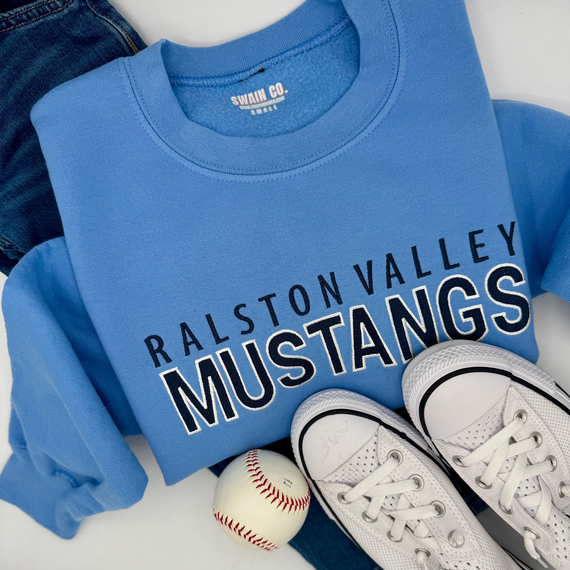 Blue sweatshirt with 'Ralston Valley Mustangs' text, white sneakers, and baseball on a light background