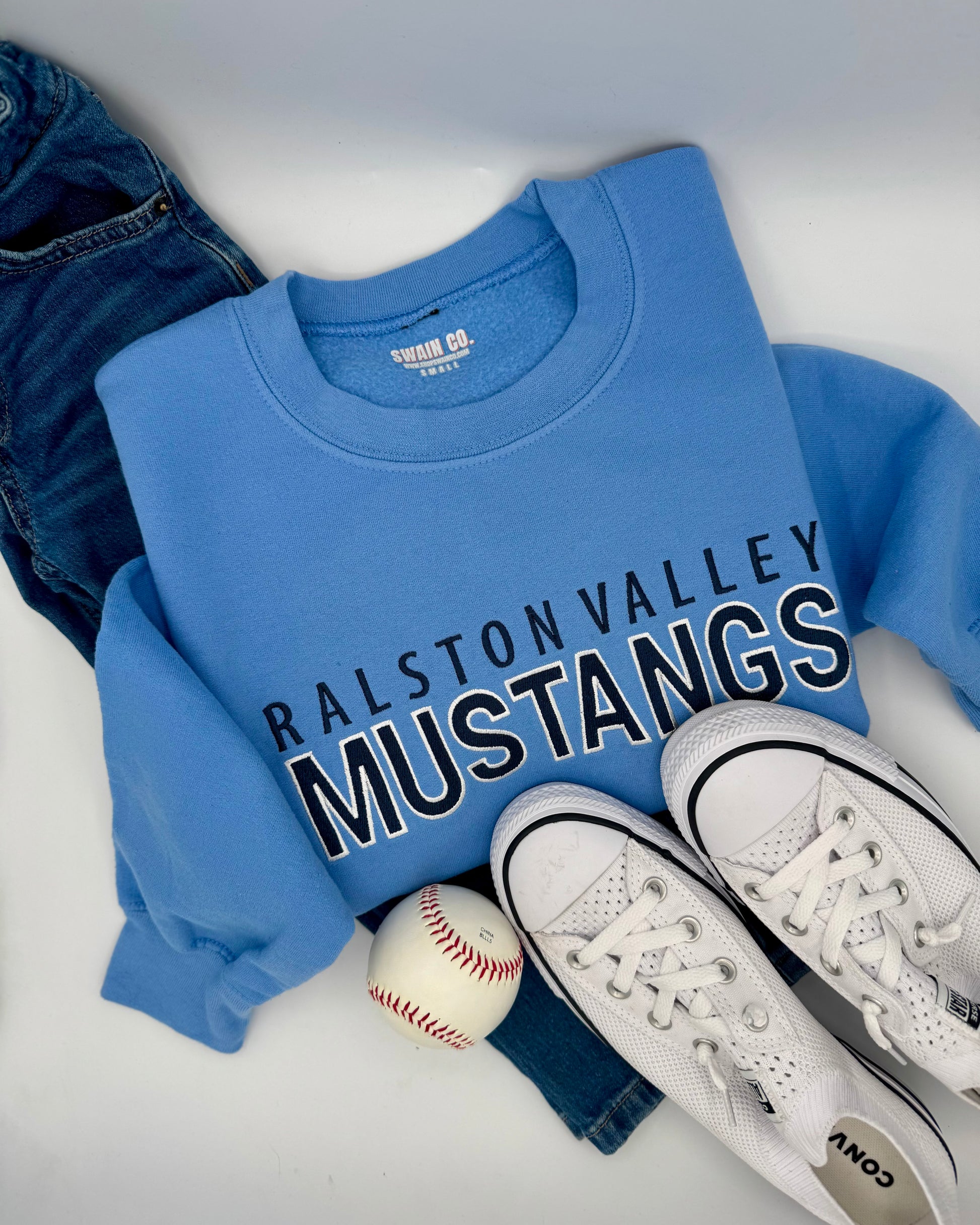Blue sweatshirt with 'Ralston Valley Mustangs' text, white sneakers, and a baseball on a light gray background